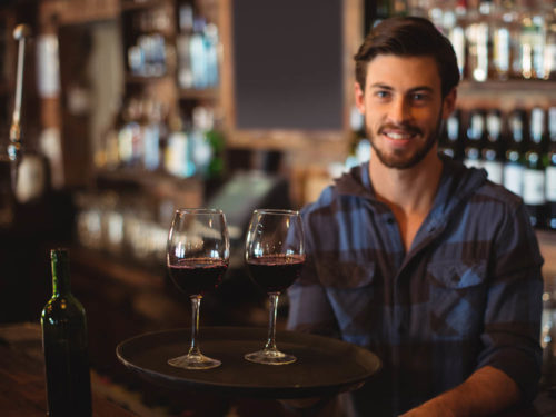 Junger Weinbarbesitzer mit zwei Gläsern Rotwein, der Dinapay, die Cloudkasse für deine Bar benutzt.